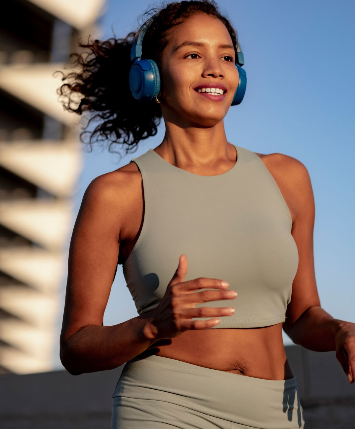 Woman jogging with headphones outdoors in sunlight.