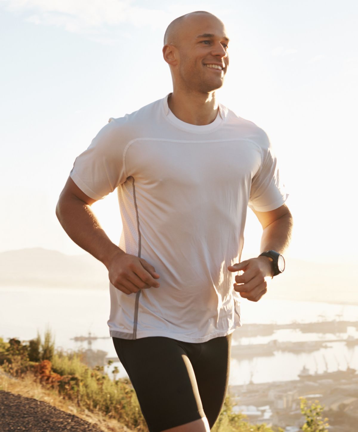 Smiling man jogging outdoors in morning sunlight.
