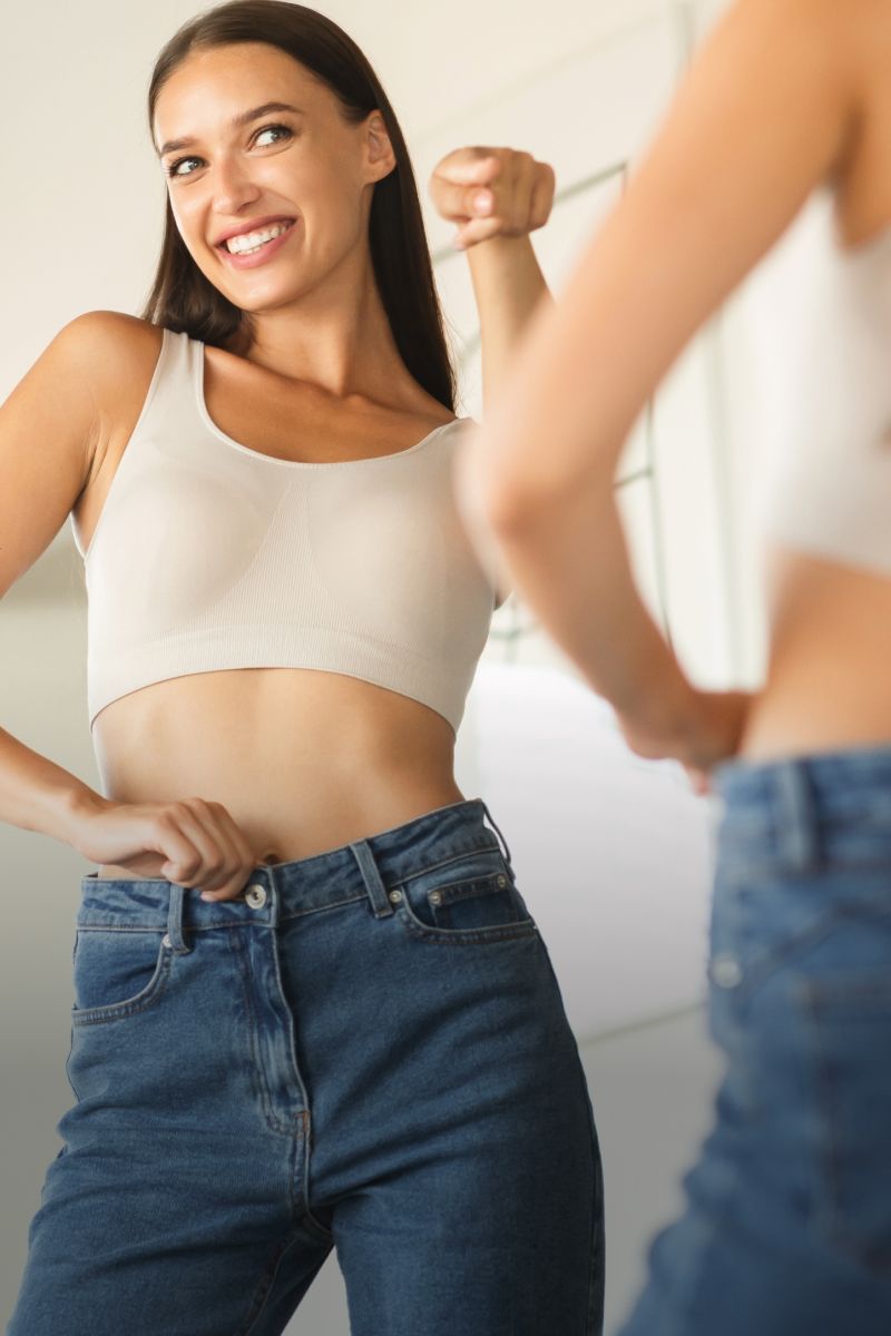 Woman smiling while adjusting her jeans in mirror.