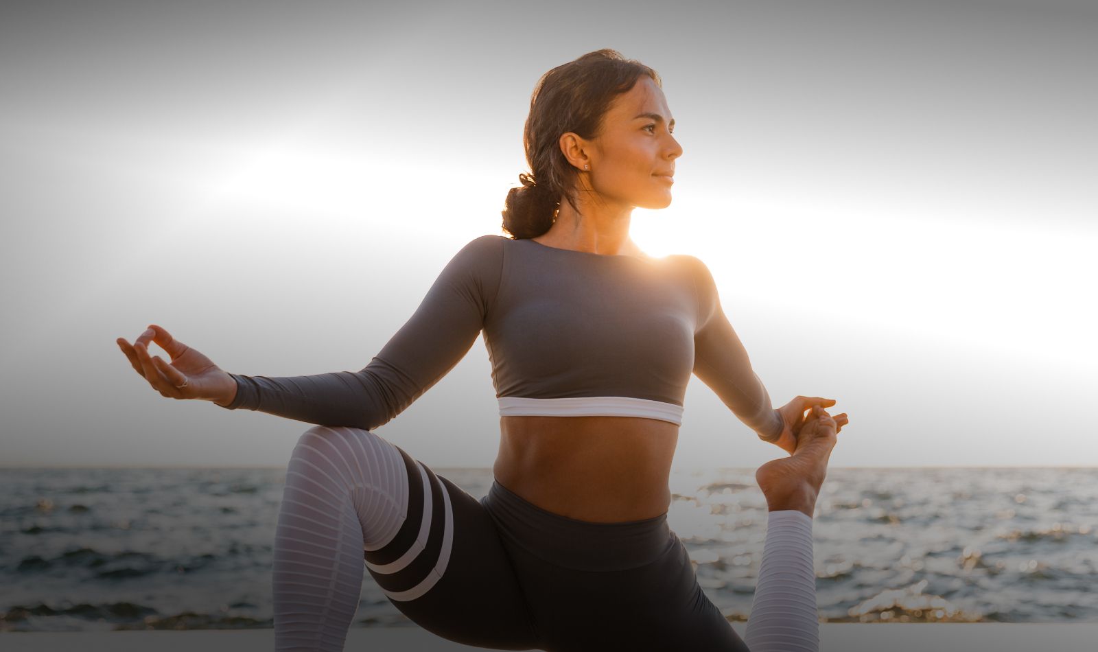 Woman practicing yoga by the ocean at sunset.