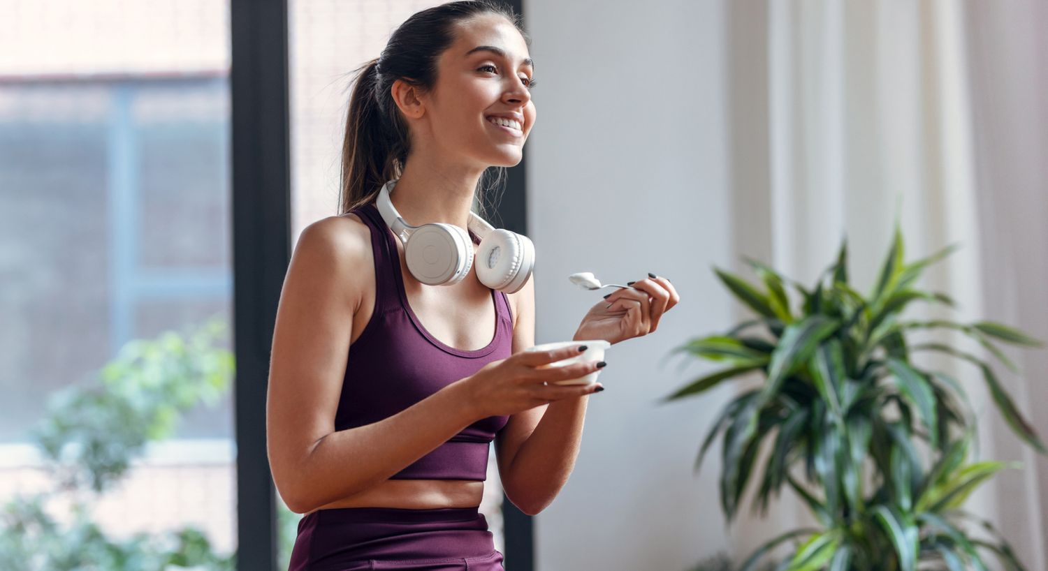  A woman in workout clothing enjoys a cup of yogurt.